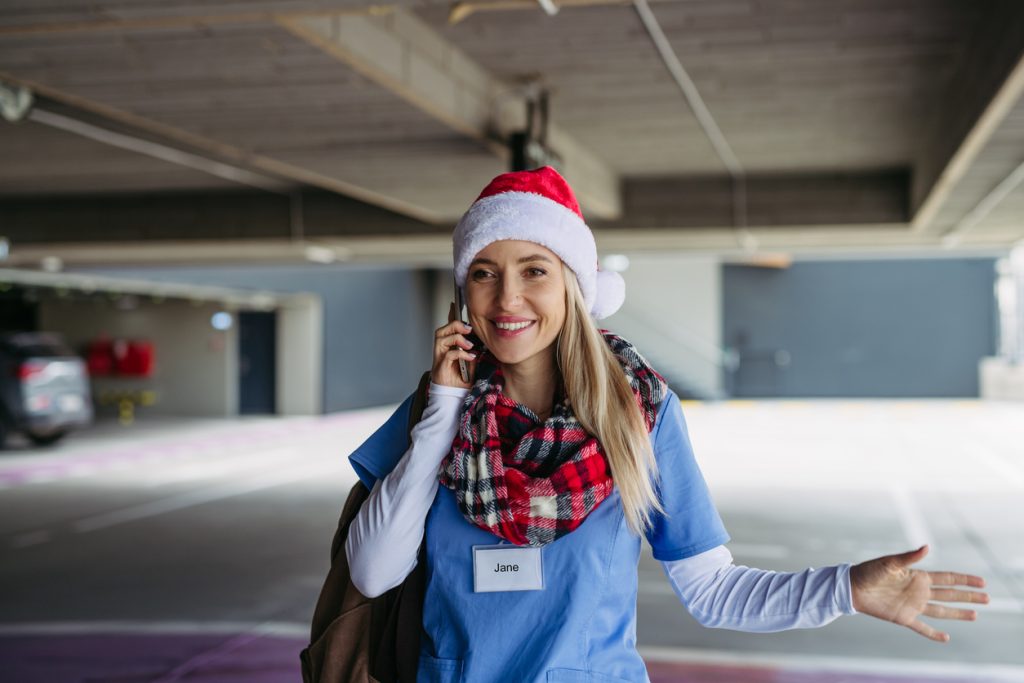 a female care worker in scrubs and a christmas hat on the phone to someone